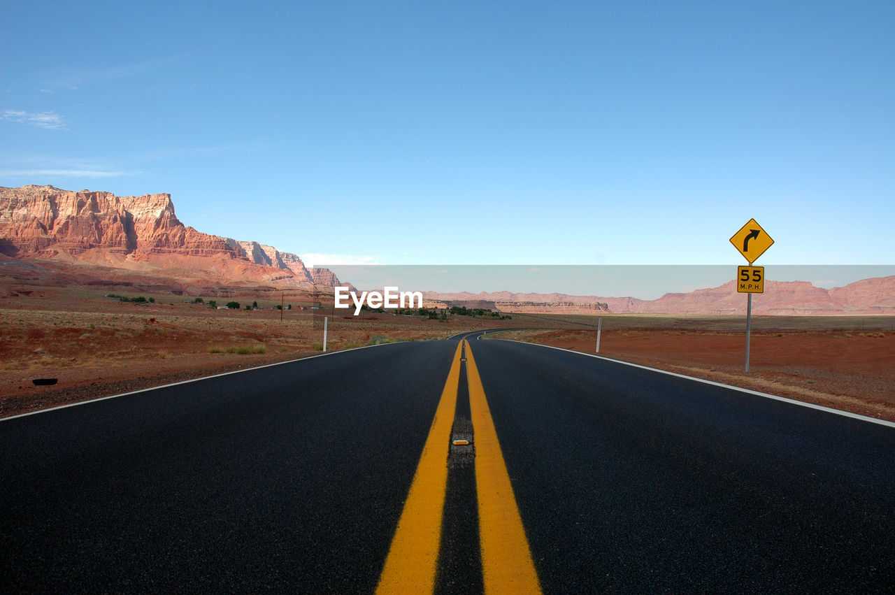 Road leading towards mountain against blue sky