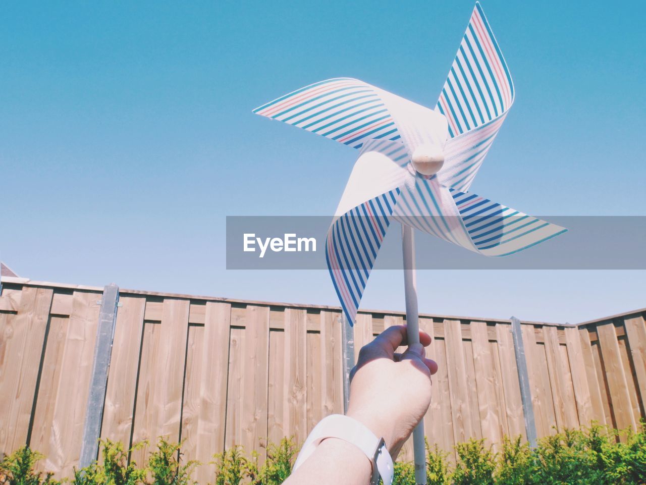 Low angle view of cropped hand holding pinwheel toy against clear sky