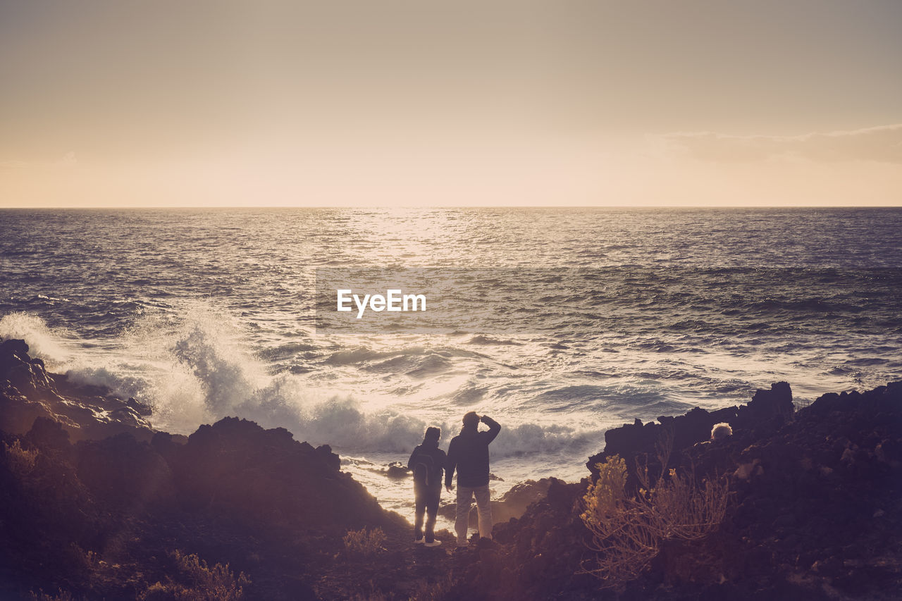 Couple standing on shore at beach against blue sky