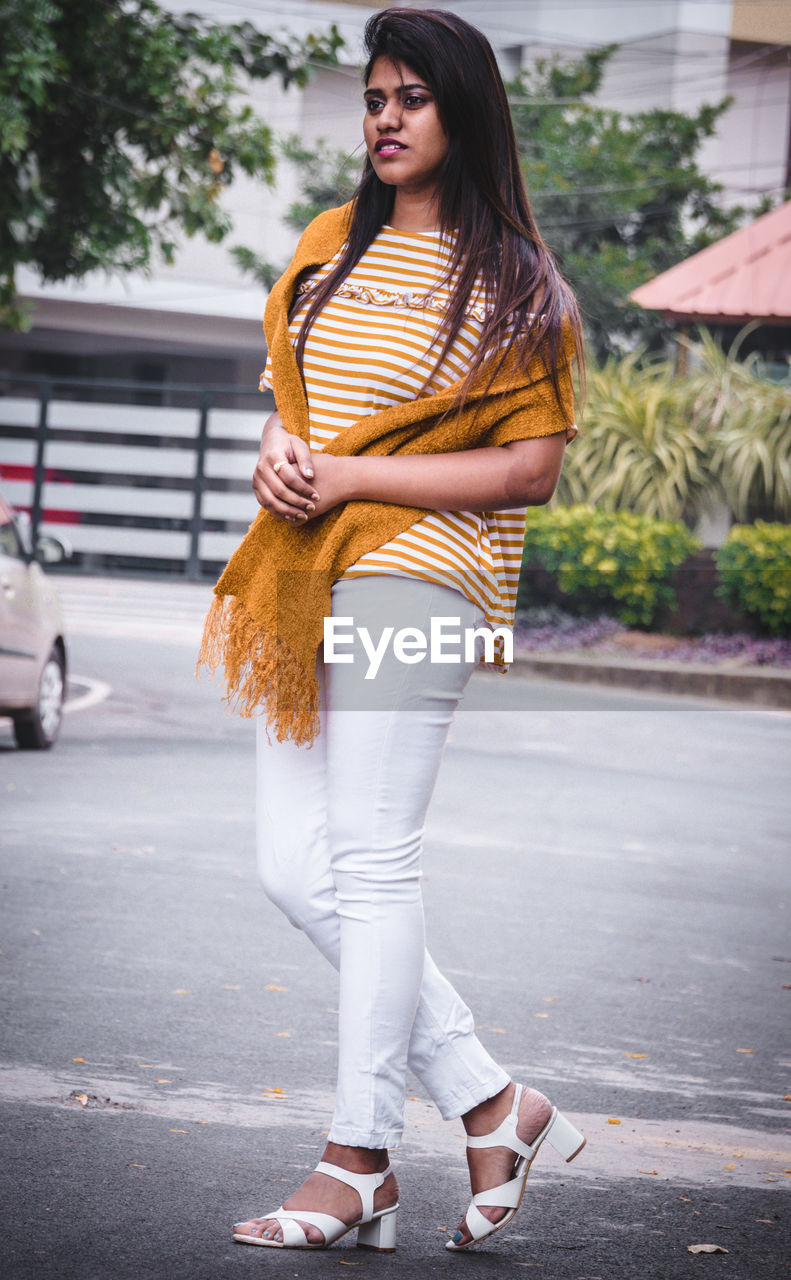 Portrait of young woman standing on road in city