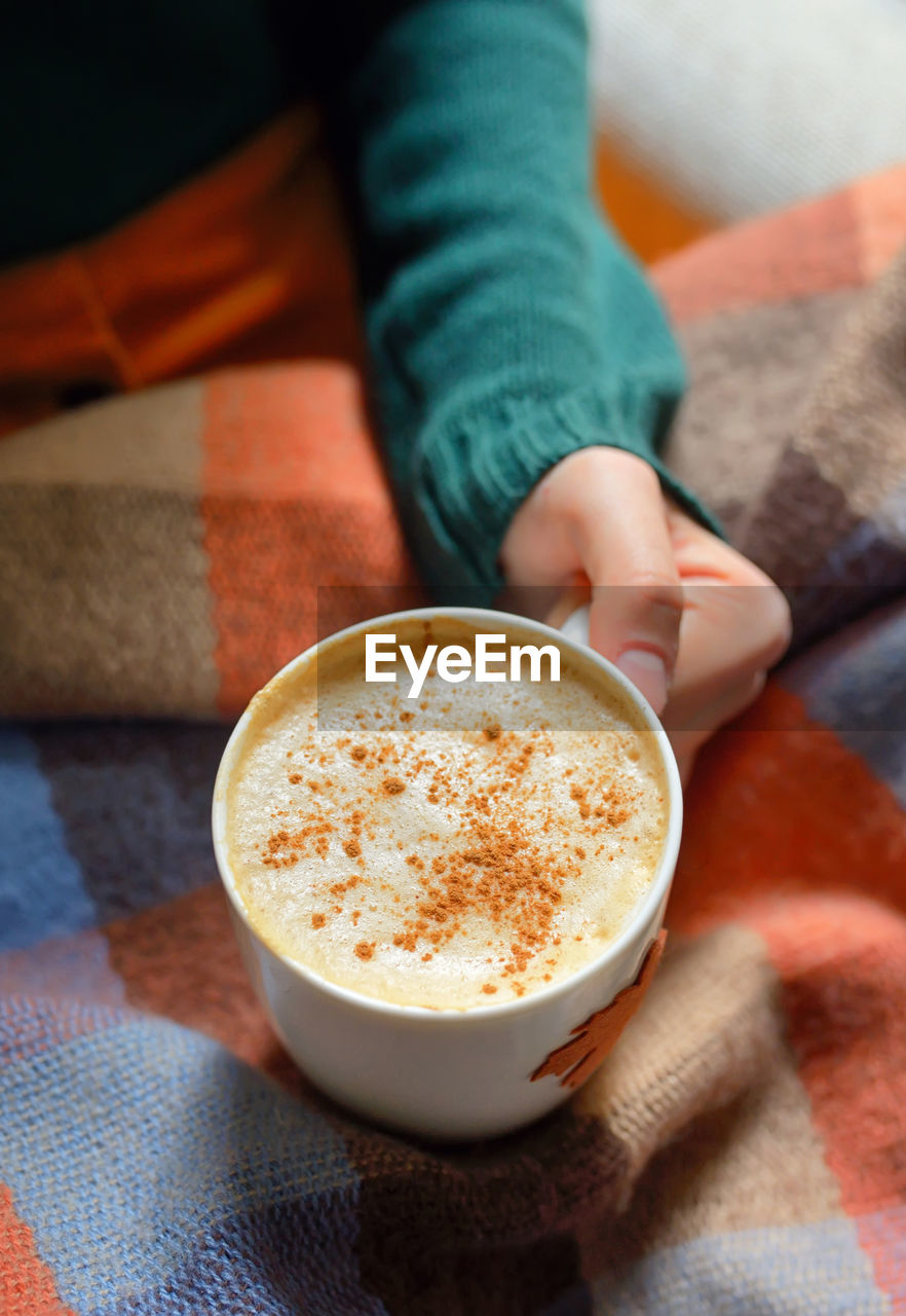 Cropped hand of woman holding coffee on bed