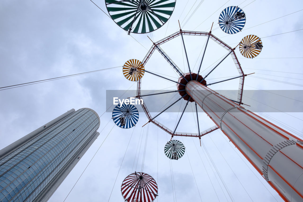 Low angle view of chain swing ride by building against cloudy sky