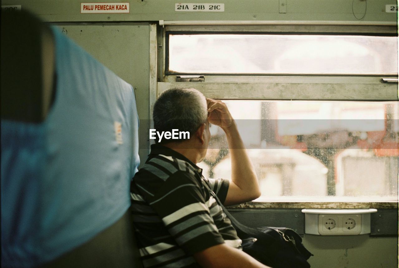 REAR VIEW OF MAN SITTING IN TRAIN AT BUS