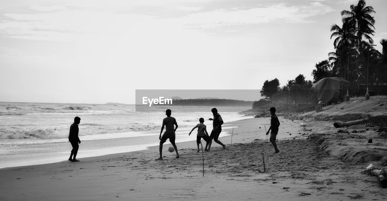 Silhouette friends playing soccer at beach