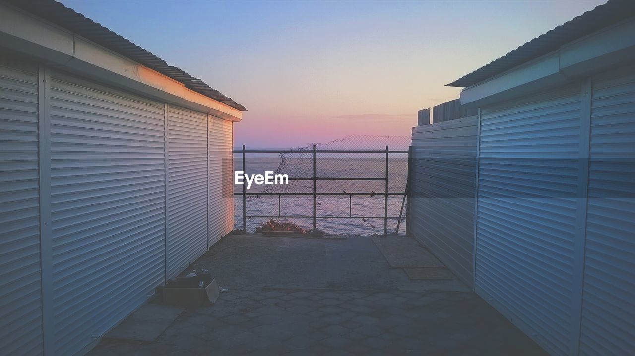 Walkway amidst houses leading toward fence during sunset