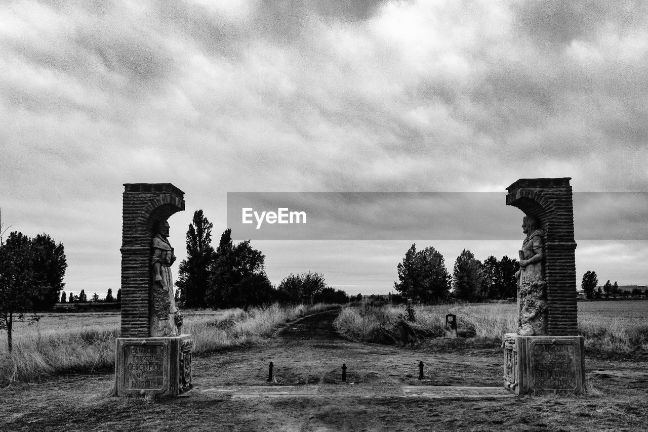 Statues on field at camino de santiago against cloudy sky