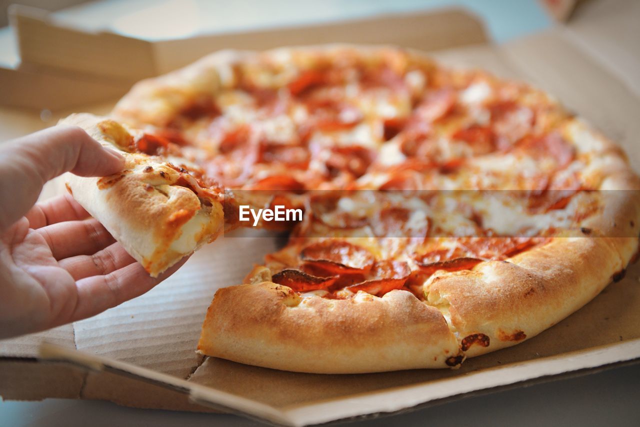 Cropped hand holding pizza on table