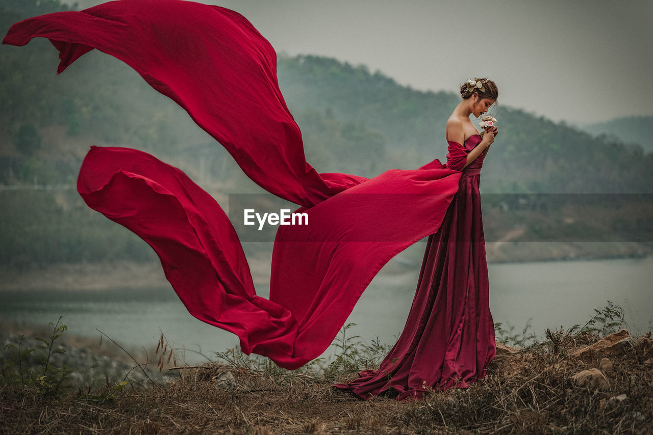 Side view of woman wearing red gown by lake