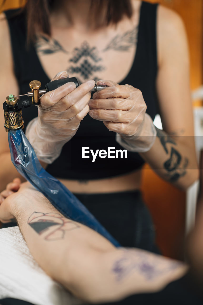 Female tattoo artist prepares tattoo machine for making a tattoo on a mens arm