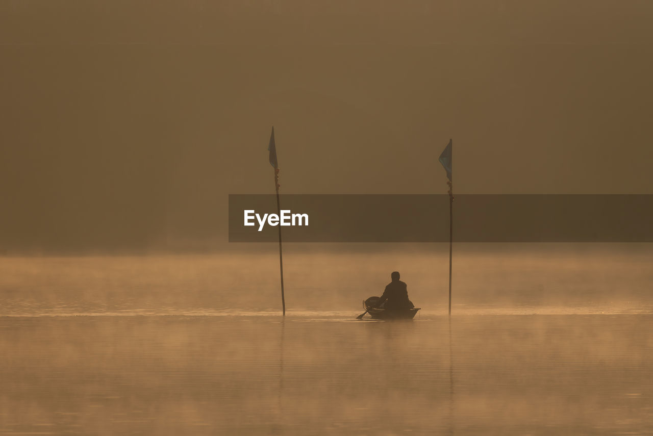 Silhouette of man sitting in boat on lake during sunset