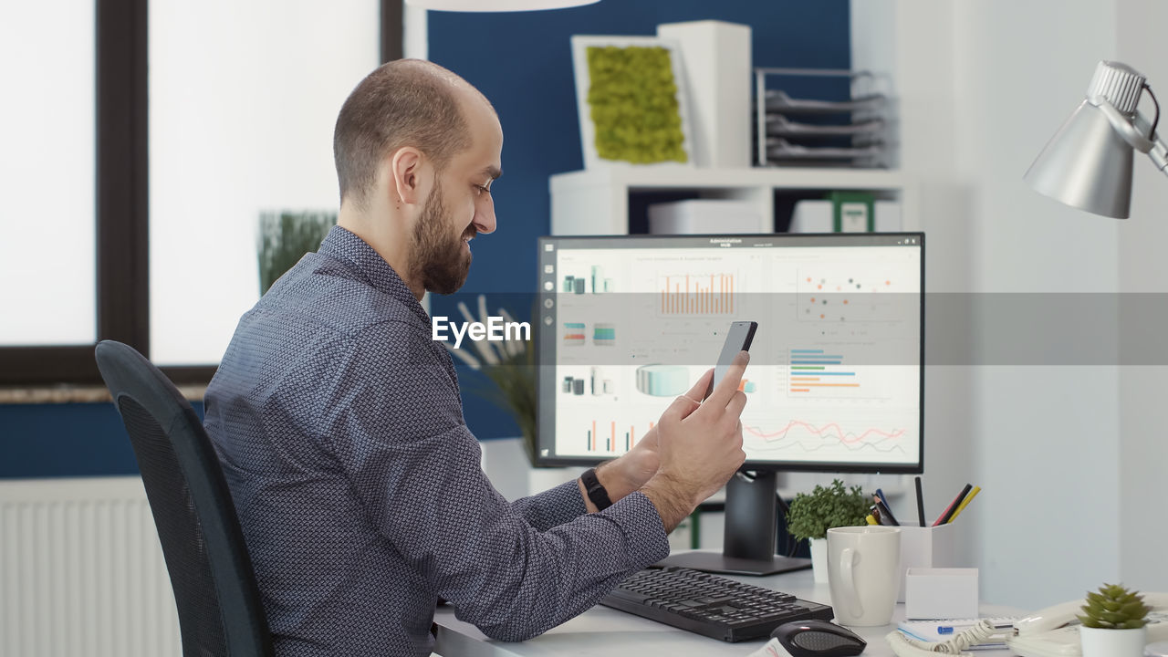 Side view of man using mobile phone while working at office