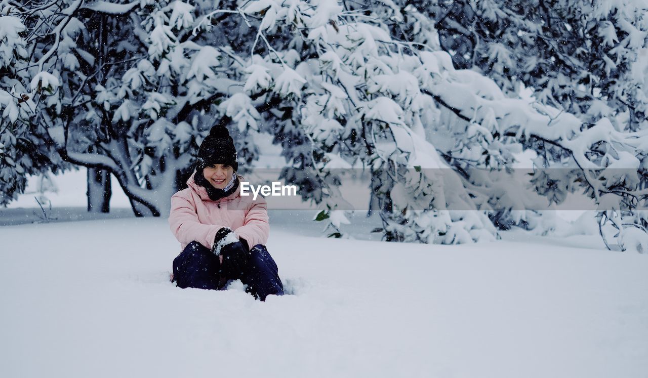 Woman sitting on snow covered land and tree