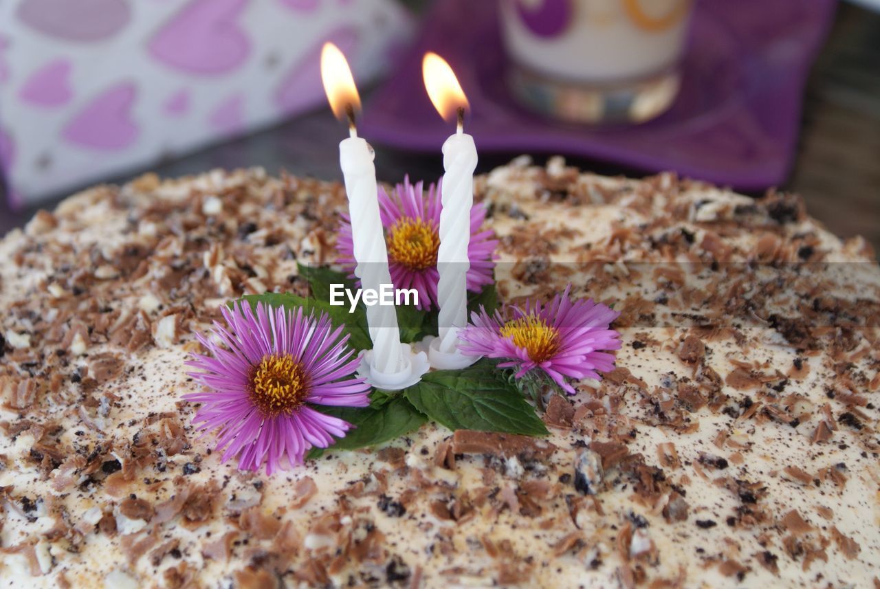 Close-up of burning candles and purple flowers on birthday cake