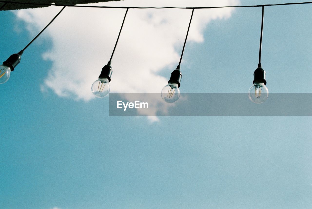 Low angle view of light bulbs hanging against blue sky