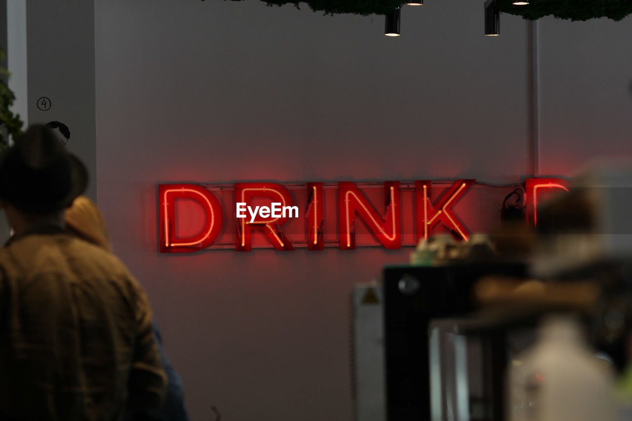 REAR VIEW OF MAN STANDING ON ILLUMINATED SIGN AT NIGHT