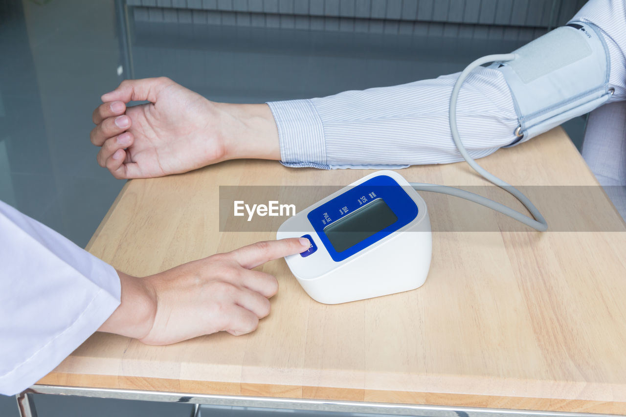 Cropped hand of doctor checking blood pressure of male patient at table