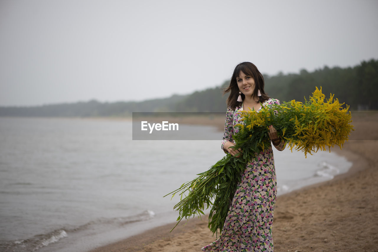 Young beautiful woman with a large bouquet of wild flowers posing on the beach