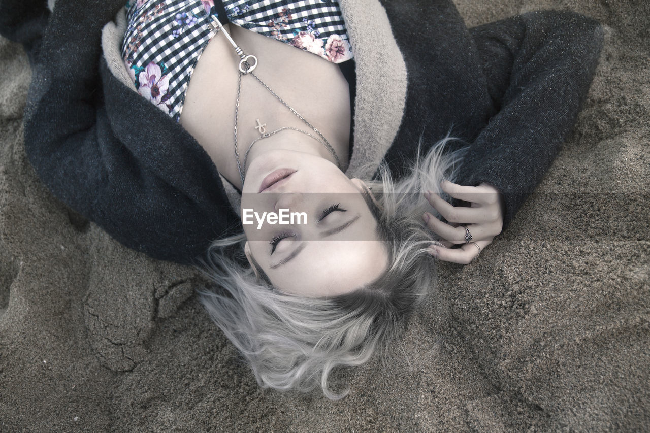 High angle view of beautiful young woman wearing chain with key pendant while lying on sand at beach