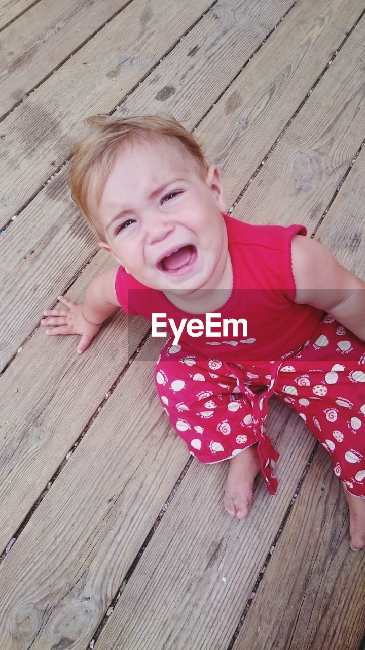 High angle portrait of toddler girl crying on boardwalk