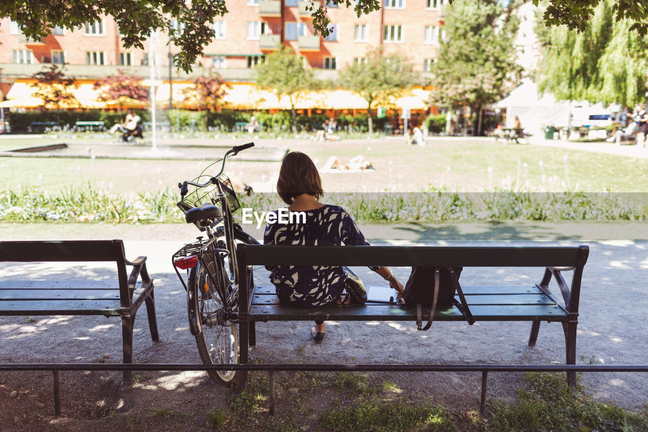 Rear view of businesswoman sitting on park bench by bicycle