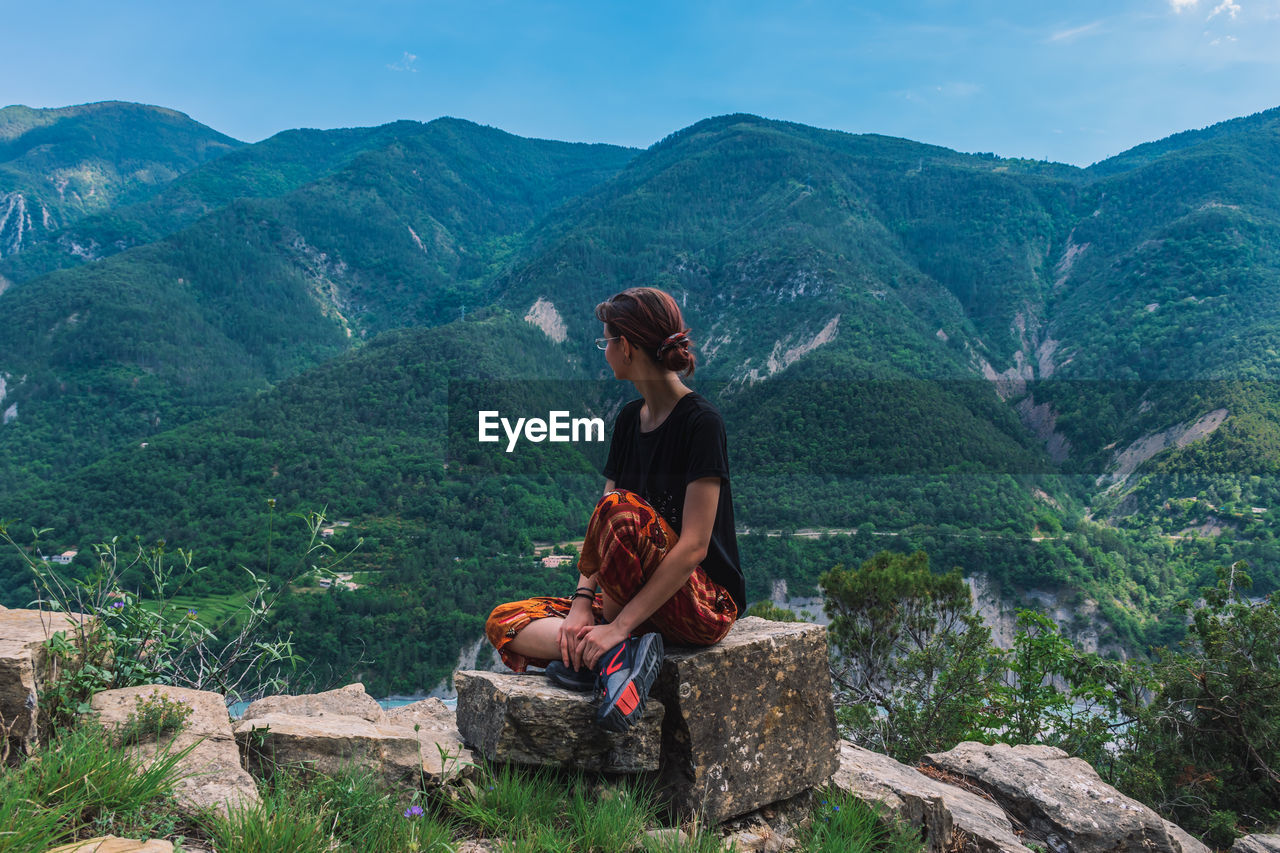 WOMAN SITTING ON MOUNTAIN LOOKING AT MOUNTAINS