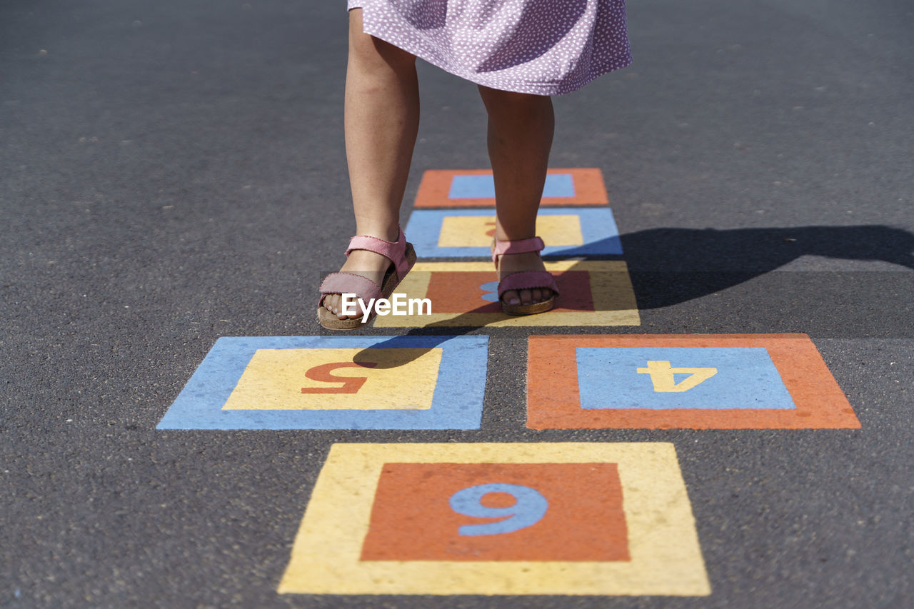 Girl playing hopscotch on footpath with numbers