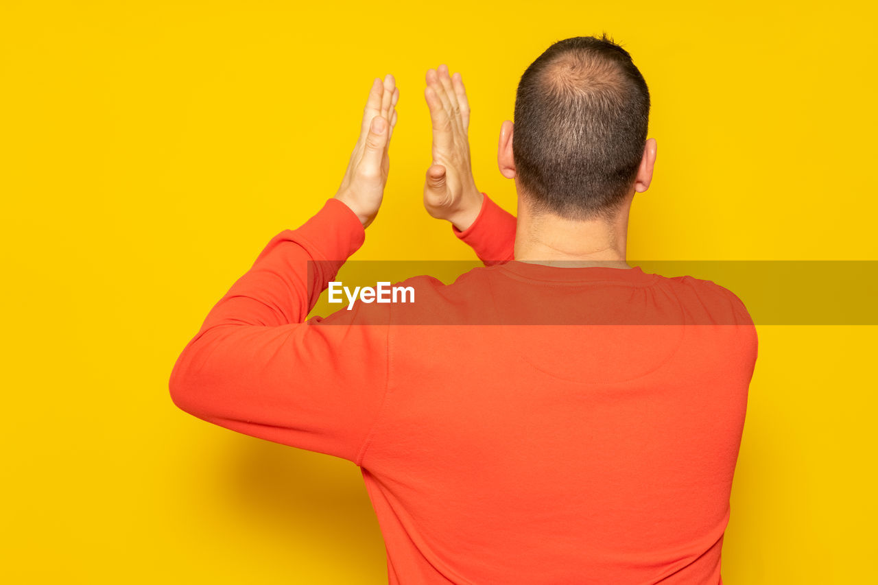 yellow, one person, rear view, adult, studio shot, colored background, orange, men, yellow background, waist up, indoors, arm, person, hand, orange color, young adult, vibrant color, portrait, clothing, casual clothing, red, finger, copy space, cut out, emotion, lifestyles, t-shirt, standing, limb