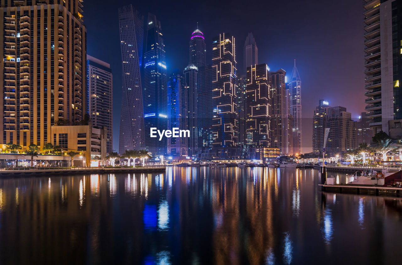 Night city dubai in uae. illuminated buildings by river against sky in city at night