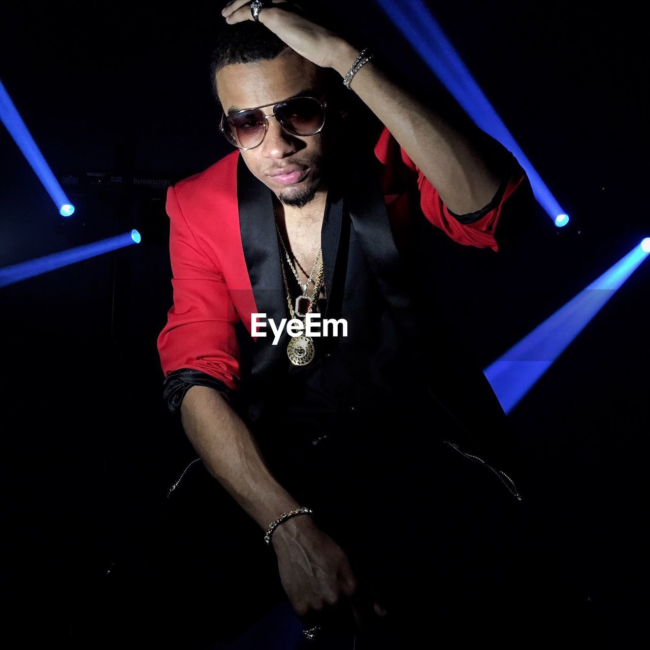 Young man in sunglasses sitting in illuminated nightclub