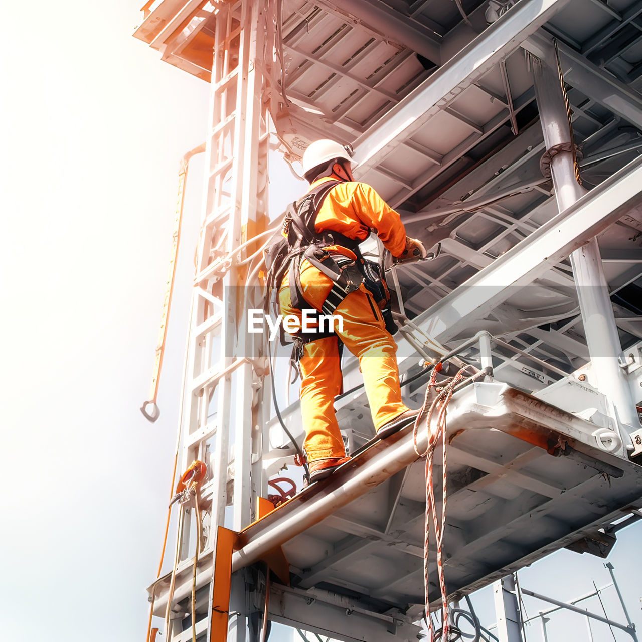 occupation, headwear, helmet, working, industry, protection, protective workwear, men, low angle view, adult, manual worker, hard hat, hat, architecture, reflective clothing, person, one person, built structure, clothing, safety harness, security, full length, skill, construction industry, business, professional occupation, occupational safety and health, standing, mature adult, communication, expertise, building, outdoors, construction site, sign, warning sign, business finance and industry, ladder, day