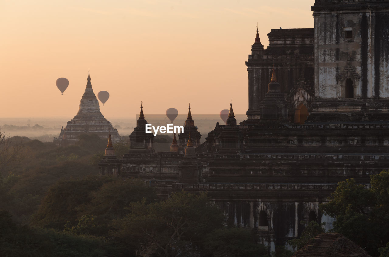 Hot air balloons flying over temple against sky