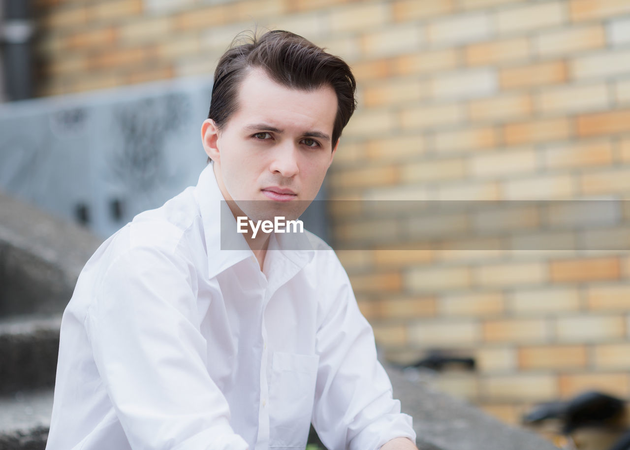 Portrait of young man sitting against brick wall