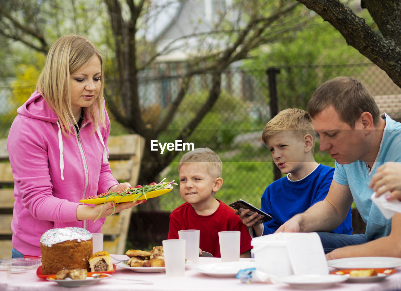 Woman serving food to sons and man outdoors