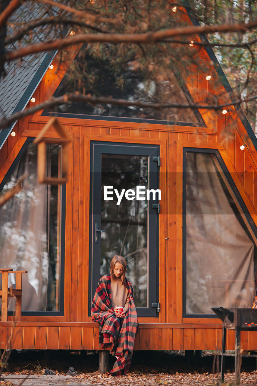 Full length of girl sitting against wooden house