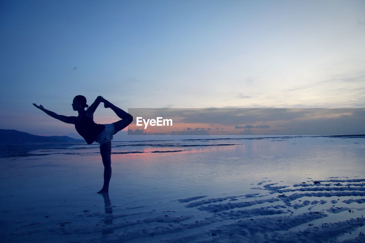 FULL LENGTH OF MAN STANDING ON BEACH AGAINST SKY DURING SUNSET