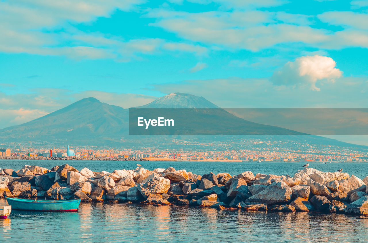 View of mount vesuvius and the gulf of naples with rocks and blue boat. naples, italy