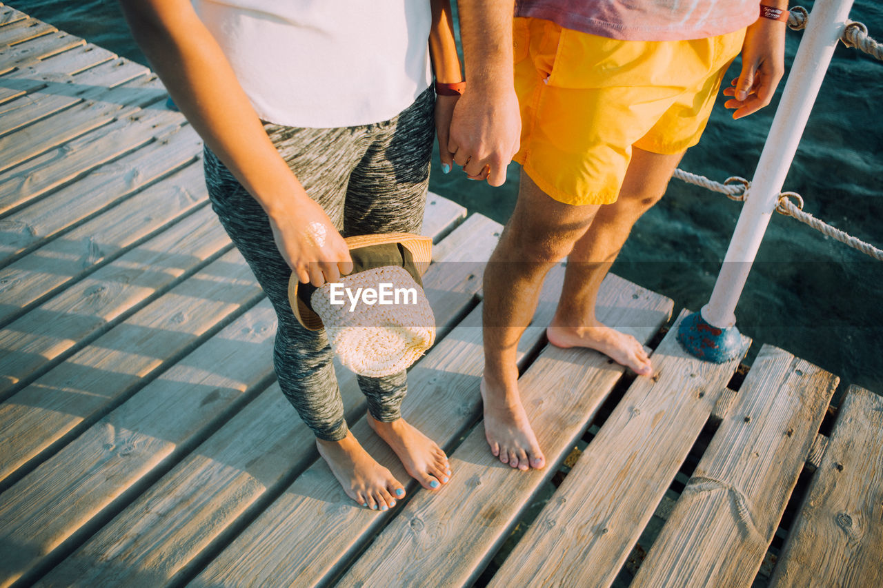 Low section of couple standing on boardwalk while holding hands