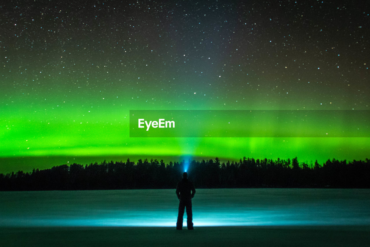 Full length rear view of silhouette man standing against sky at night with northern lights