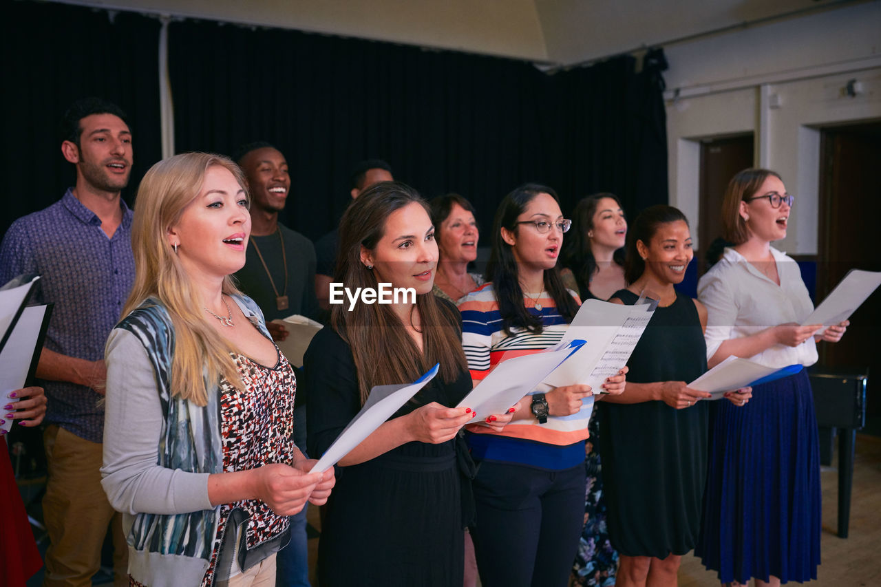 Male and female friends practicing choir on stage in auditorium