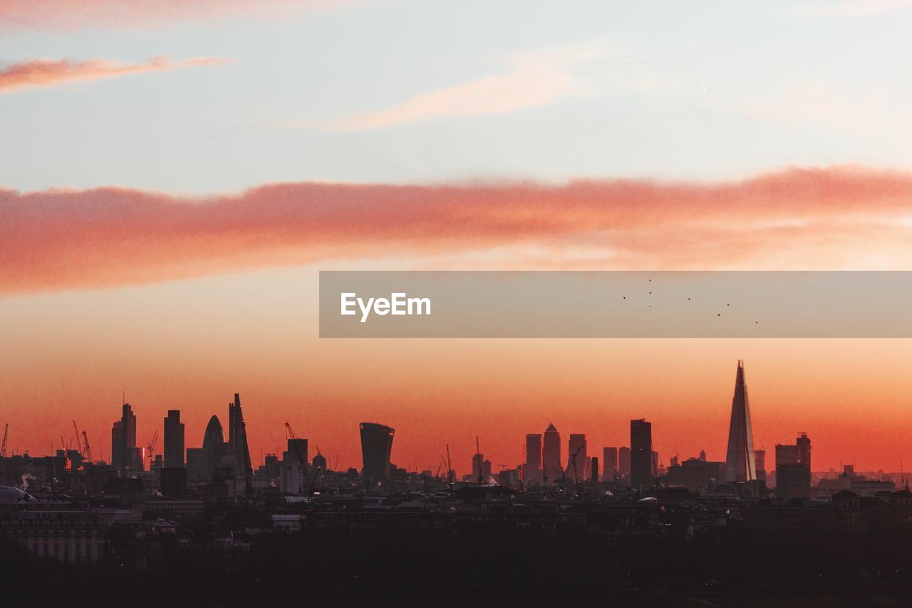 Modern buildings against cloudy orange sky during sunrise