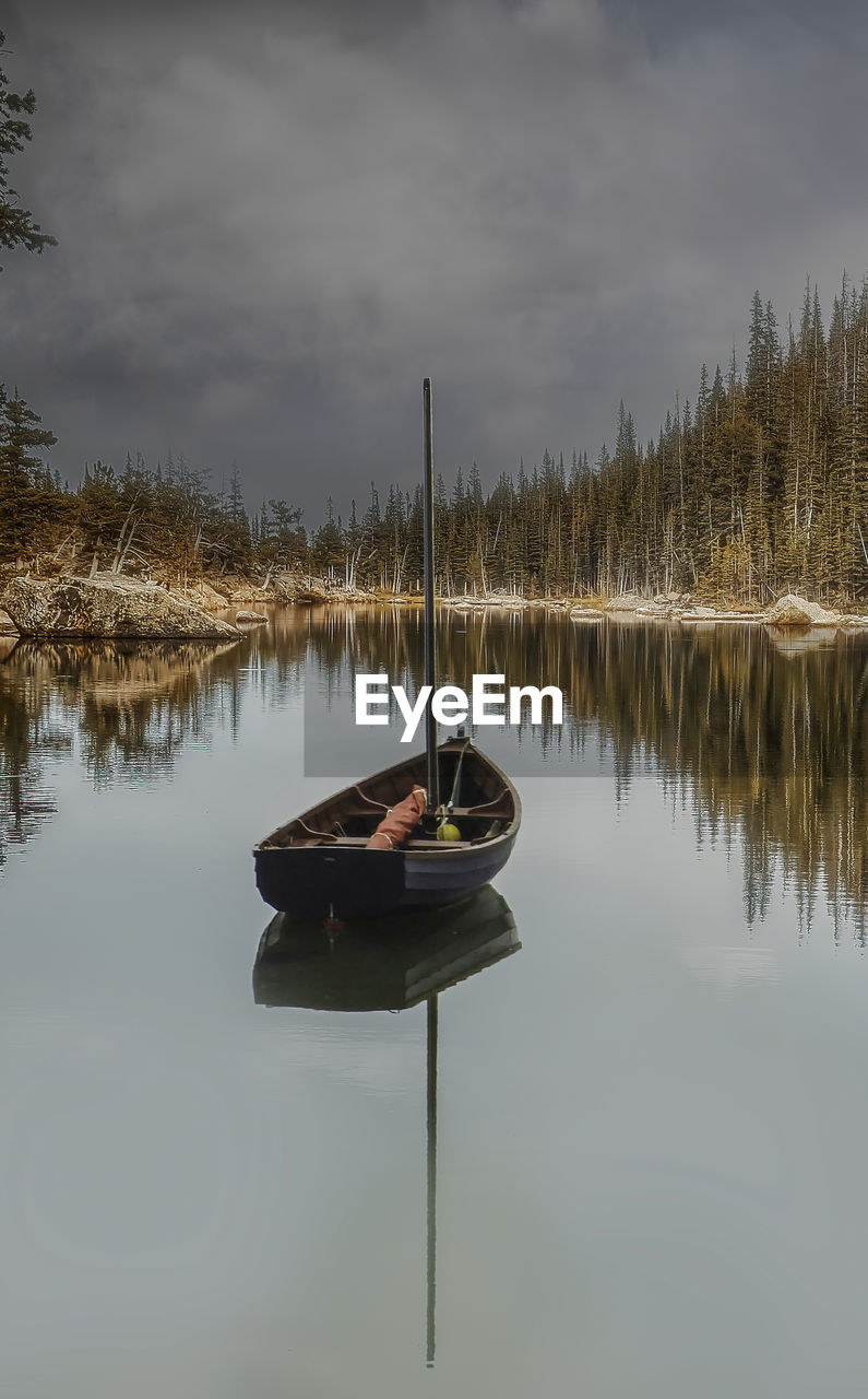 MAN SITTING ON LAKE AGAINST SKY