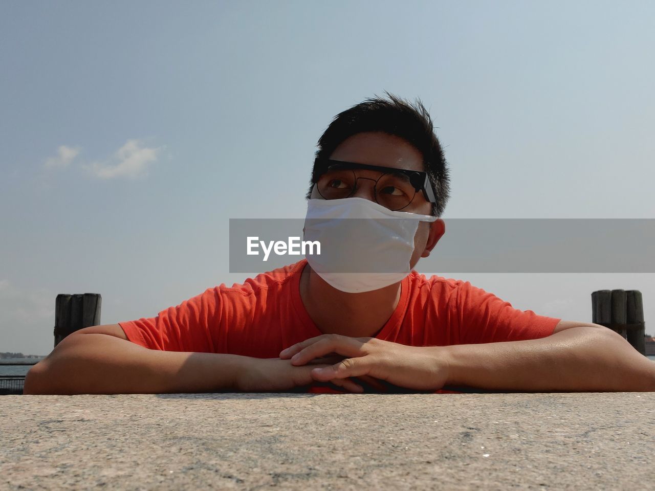 PORTRAIT OF YOUNG MAN WITH SUNGLASSES SITTING AGAINST SKY