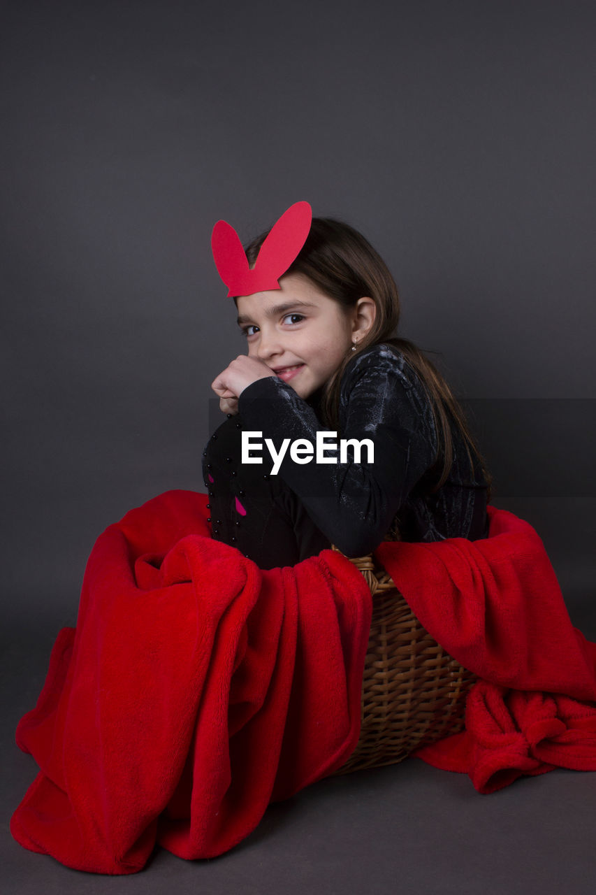 Portrait of smiling girl with costume rabbit ears sitting in basket against gray background