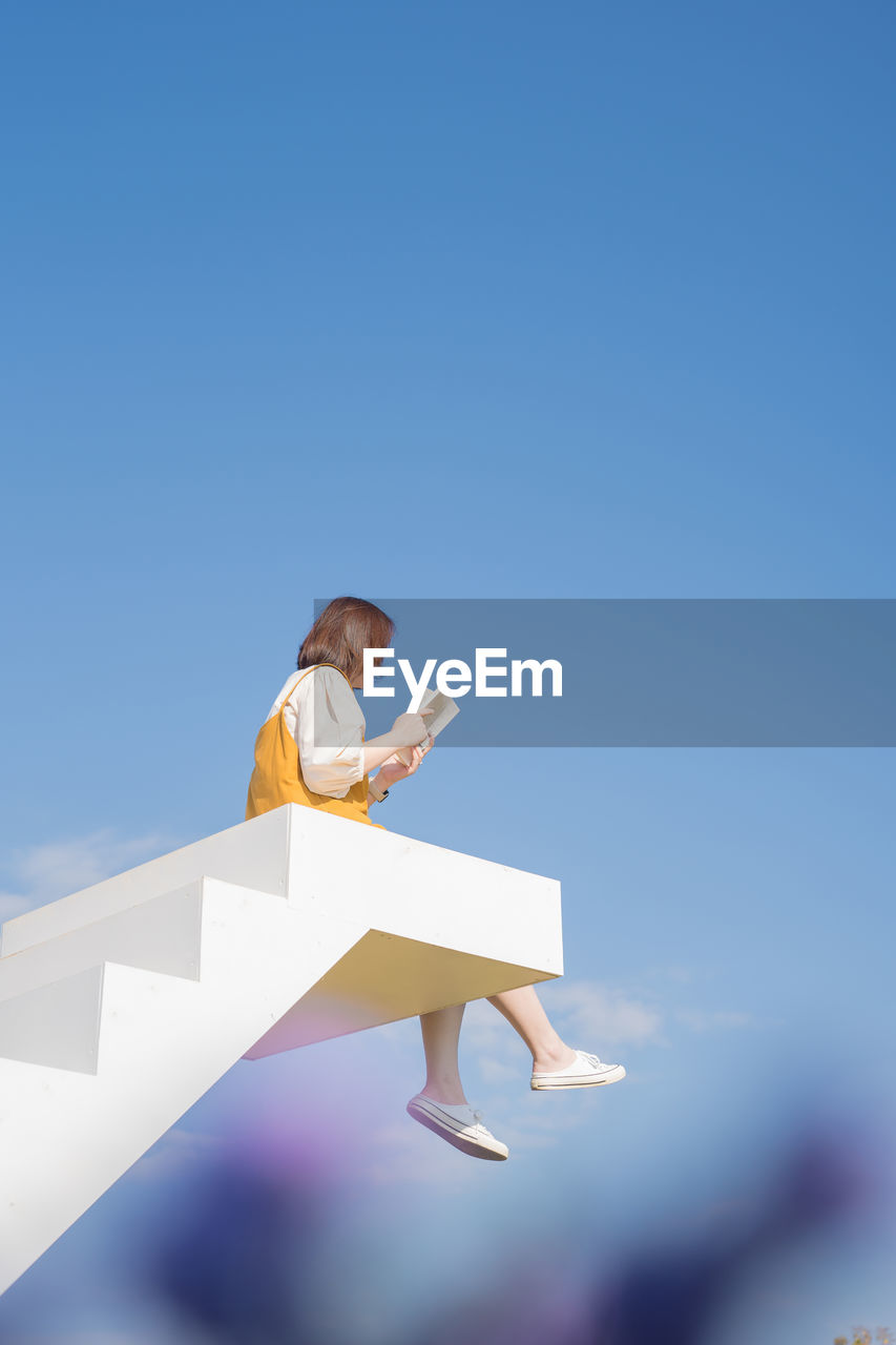 Asian woman relax and reading on white stair in flower garden on springtime vacation