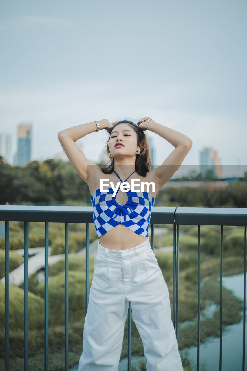 Portrait of young woman standing against railing