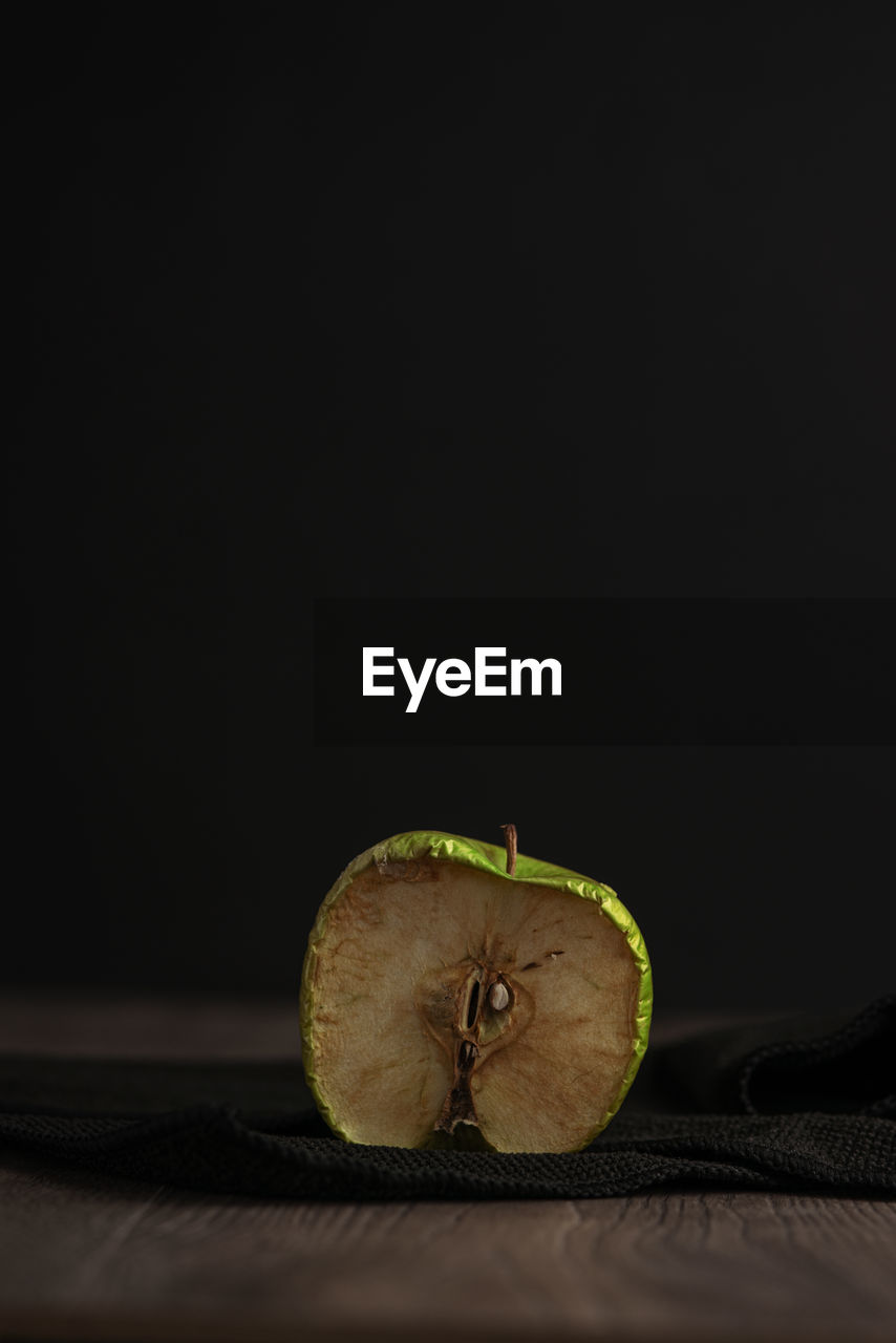Withered green apple cut in half placed on wooden table against black background