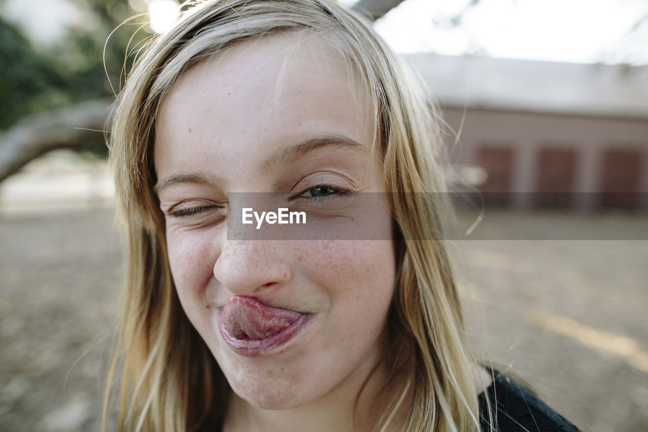 Close-up portrait of playful girl sticking out tongue while winking at farm