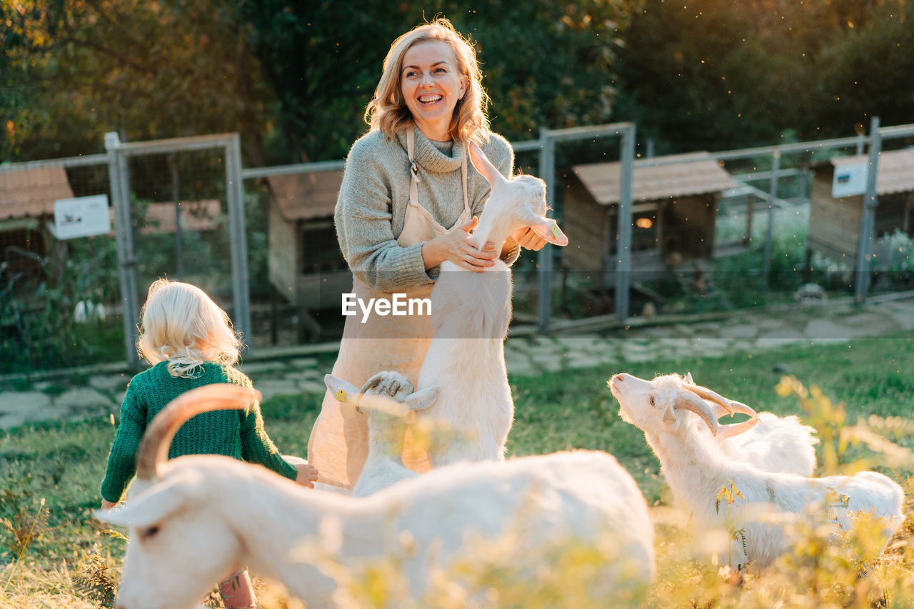 Happy smiling woman and little girl feed goats on the farm. rural life, recreation with animals.