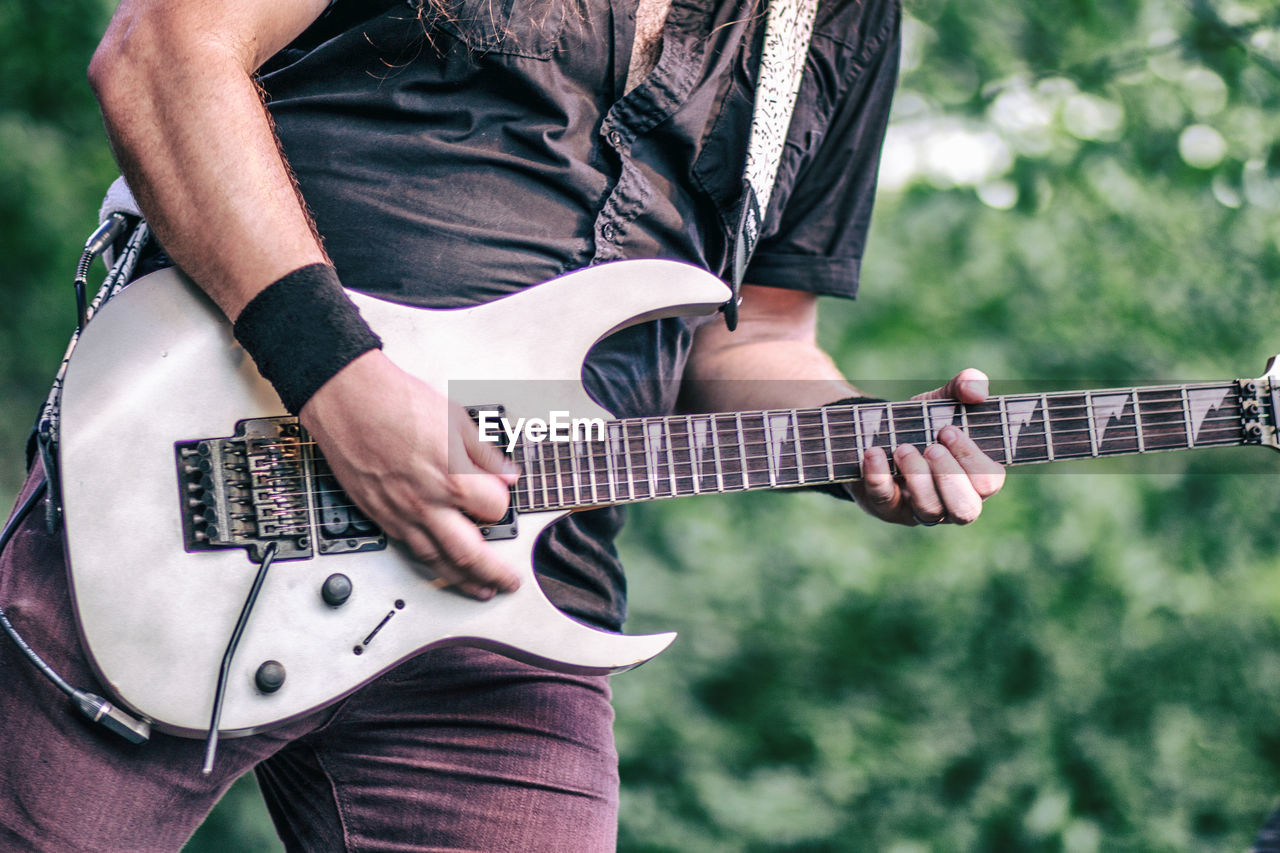 Midsection of man playing guitar while standing outdoors