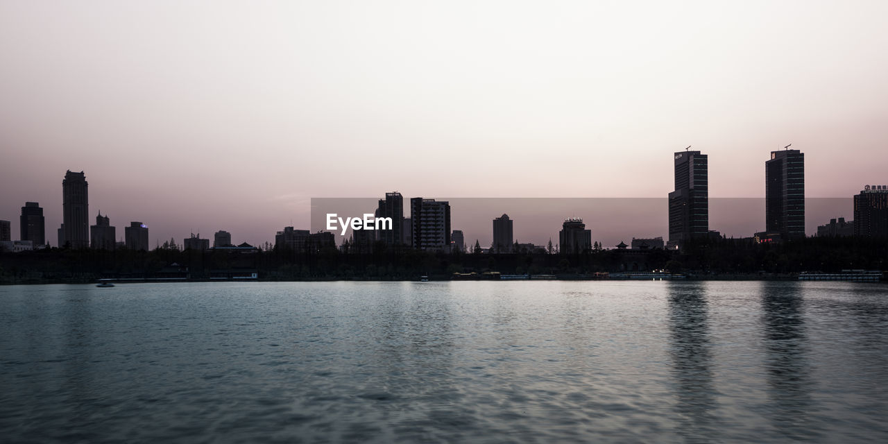 SEA BY CITY BUILDINGS AGAINST SKY DURING SUNSET